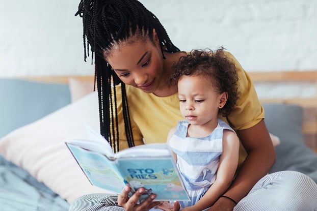 Mom reading to young daughter teaching her print awareness