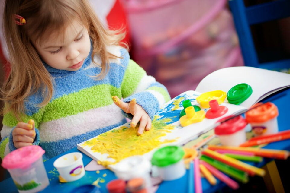 A girl painting in her nursery with finger paints