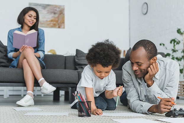 Mom reading a book on couch with dad on floor coloring with child