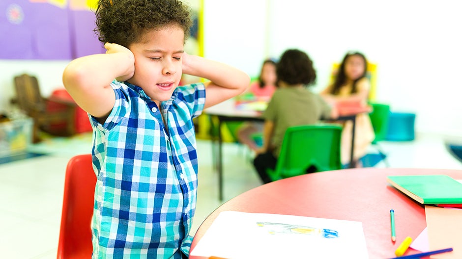 Emotionally sensitive child covering their ears in the classroom