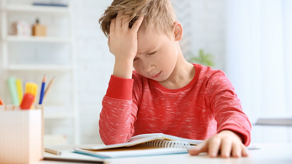Emotionally sensitive child holding head in hand while looking at notebook