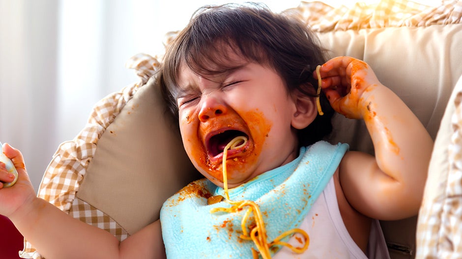 Child having temper tantrum eating spaghetti in high chair