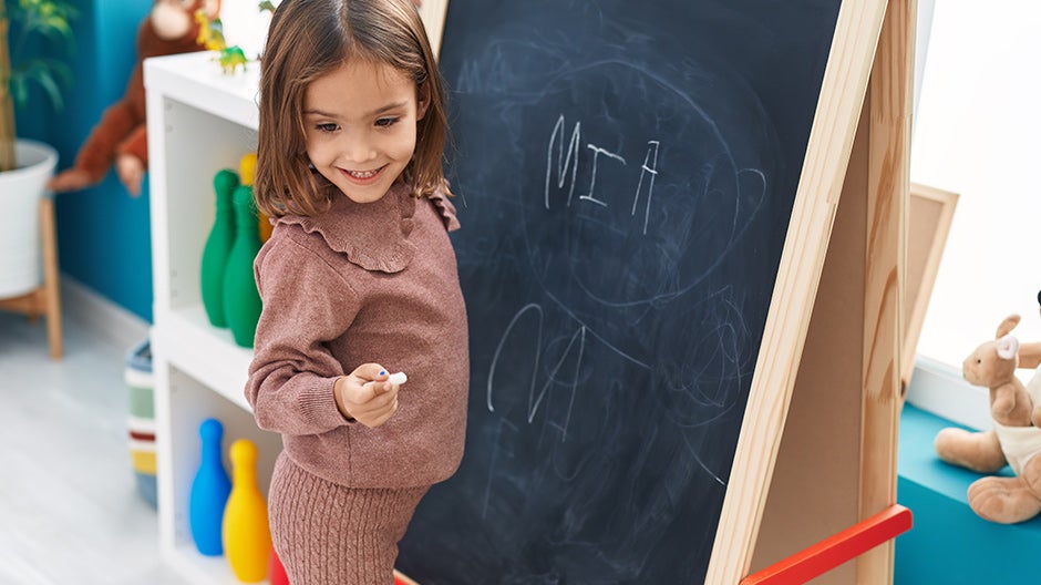 Child standing at blackboard working on learning to write