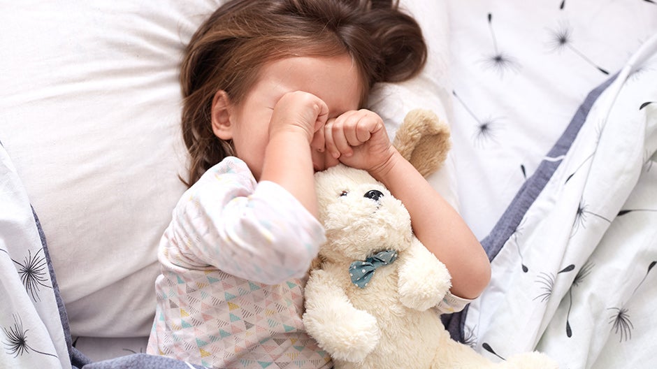 Toddler with teddy bear rubbing her eyes at bedtime