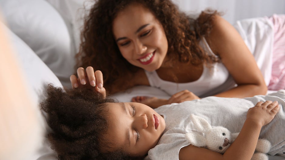 Smiling mother saying goodnight to calmly sleeping toddler at bedtime