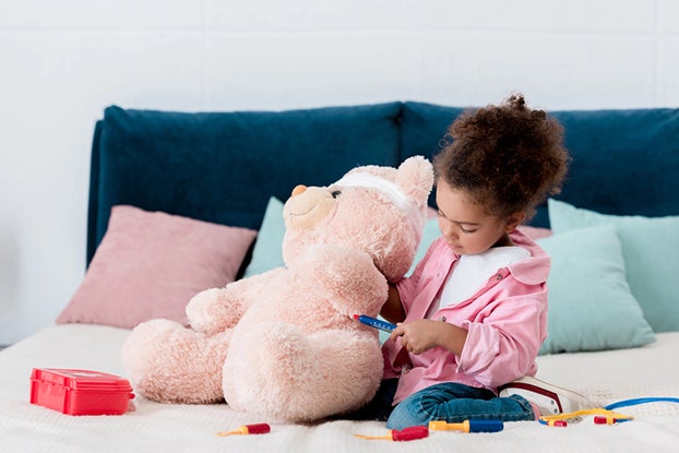 young girl in pretend play as a doctor preforming a medical task on a teddy bear
