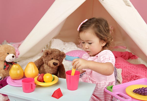 young girl playing pretend play tea party with stuffed animals