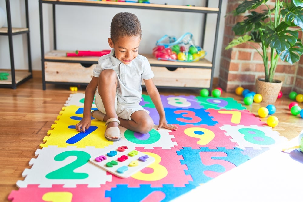 Young kid playing with wood numbers on a numbered playing mat
