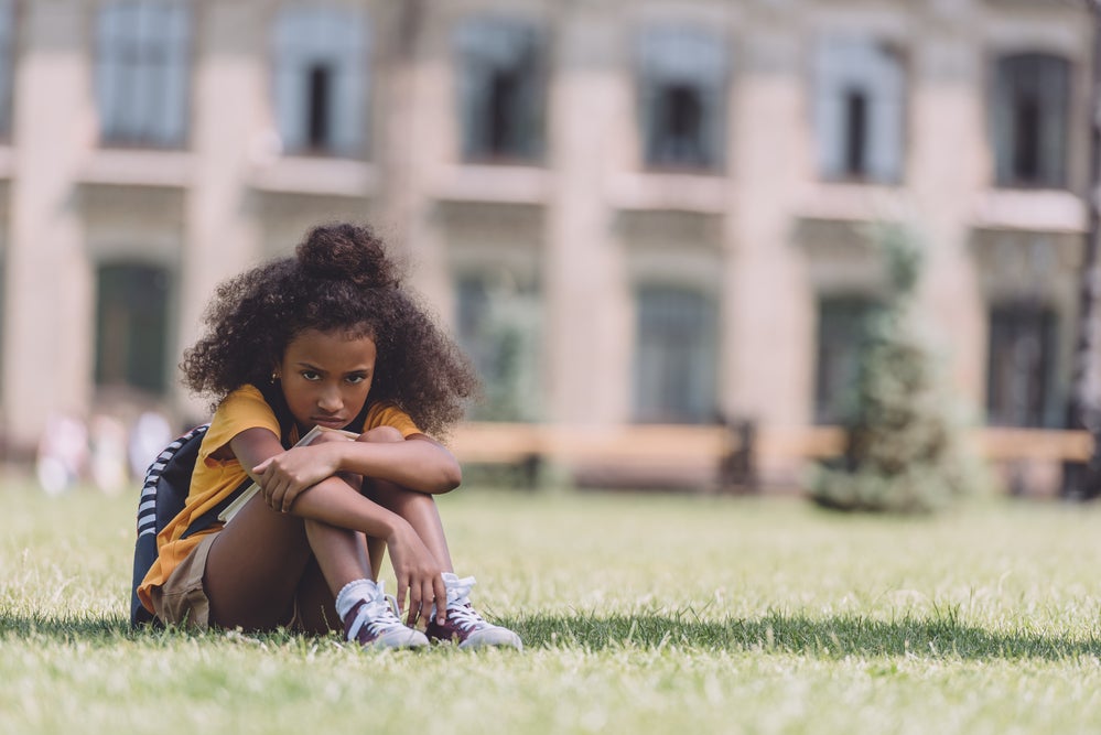 Young girl at school sitting on grass upset